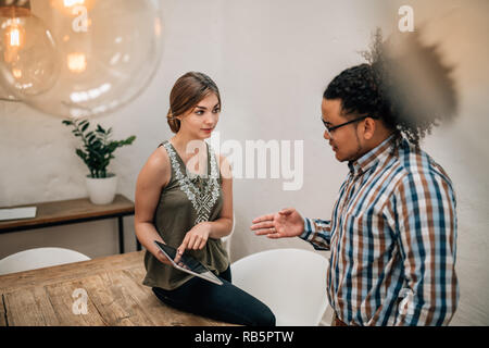 Two young creatives talking and using tablet in boardroom, the woman is pointing to a tablet and the mixed race guy is explaining Stock Photo