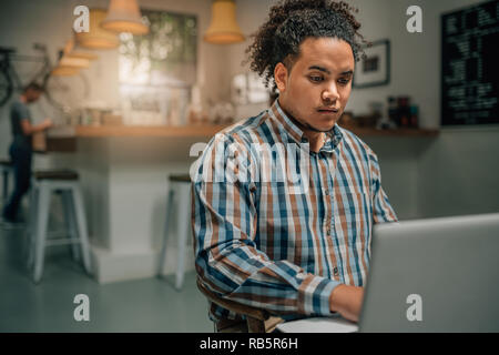 Handsome mixed race guy working on laptop in a coffee cafe Stock Photo