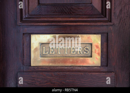 Bronze mailbox. Brass letterbox plate on a wooden front door, text letters. Closeup view with details Stock Photo
