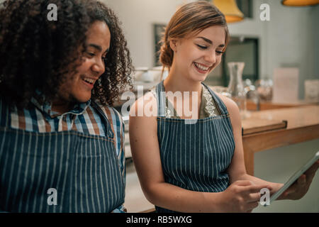Two waiters smiling and laughing at something being pointed to on a digital tablet Stock Photo