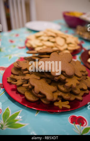 Close up of a red plate full of freshly baked christmas themed gingerbread cookies on a table with other plates full of cookies in the background Stock Photo