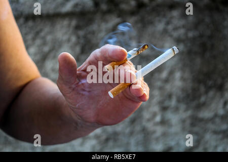 Human hand holding two cigarettes burning at the same time Stock Photo