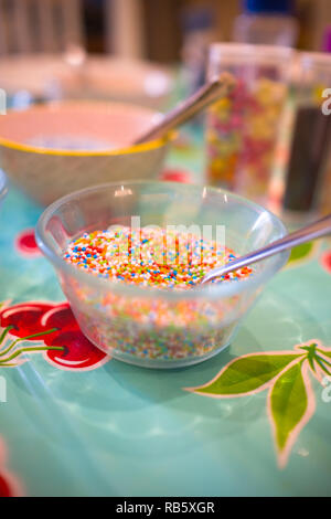 close up of glass bowl filled with edible confetti sprinkles and a spoon on a table during a cookie decorating party Stock Photo