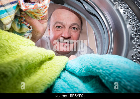 Senior man putting dirty towels in washing machine to clean them. View from washing machine inside. Everyday chore concept Stock Photo