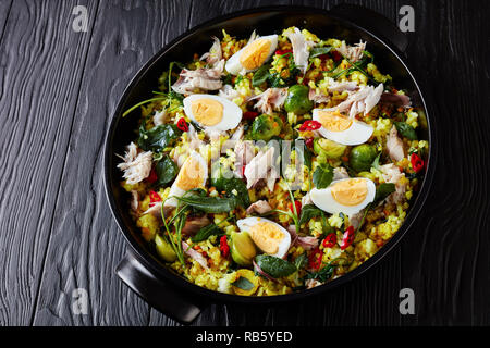 Kedgeree with flaked smoked fish, hard boiled eggs, rice, kale, brussel sprouts, spices and herbs in a ceramic pan on a wooden table, view from above, Stock Photo