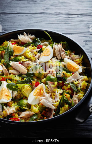 delicious Kedgeree with flaked smoked fish, hard boiled eggs, rice, kale, brussel sprouts, spices and herbs in a dutch oven on a black wooden table, v Stock Photo