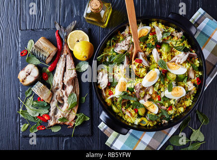 delicious Kedgeree with flaked smoked fish, hard boiled eggs, rice, kale, brussel sprouts, spices and herbs in a dutch oven on a black wooden table wi Stock Photo