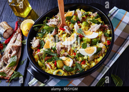 delicious Kedgeree with flaked smoked fish, hard boiled eggs, rice, kale, brussel sprouts, spices and herbs in a dutch oven on a black wooden table wi Stock Photo