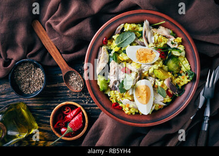 delicious Kedgeree with flaked smoked fish, hard boiled eggs, rice, kale, brussel sprouts, spices and herbs in a bowl on an old wooden table with fenn Stock Photo