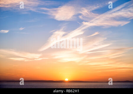 Beautiful sunrise in orange colors, sun, a blue sky with interesting cloud formation and the sea. Stock Photo