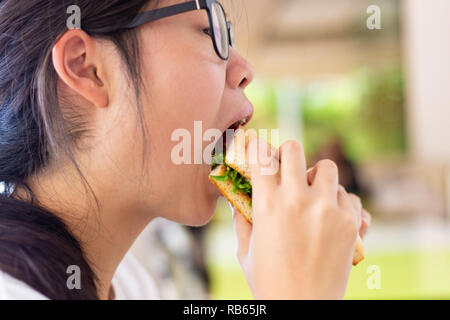 Young female teenager eating her sandwich and pizza for lunch at restaurant Stock Photo