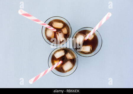 Iced coffee, ice cubes and straws in three glasses on violet background. Top View. Stock Photo
