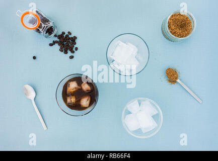 Glasses of cold brew coffee, coffee beans, sugar and a bowl filled with ice cubes on blue background. Top view. Stock Photo