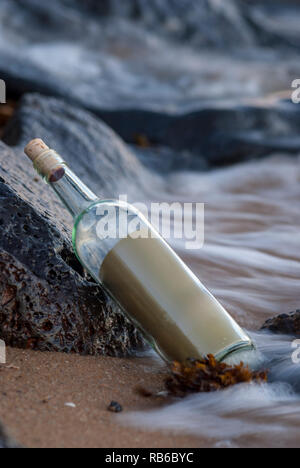 message in a bottle, washed up against the rocks on the beach Stock Photo