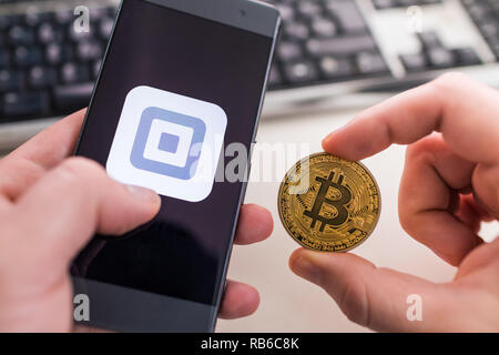 SLOVENIA - JANUARY 8, 2019: Man holding Bitcoin coin and in other hand smartphone with Square application. Stock Photo