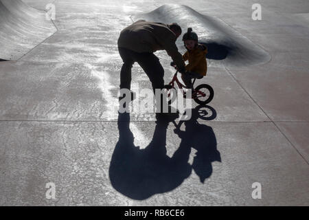 Denver, Colorado - Adam Hjermstad Sr. helps his four-year-old son, Adam Jr., to ride his balance bike in a skatepark. Stock Photo