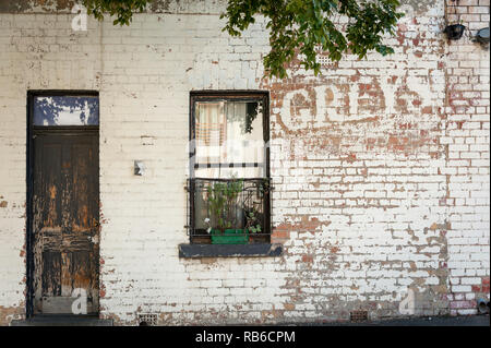 the remains of and old painted sign on the side of a building with a brown wooden door and window with planter box Stock Photo