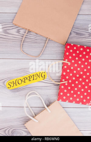 Set of shopping bags on wooden background. Kraft paper packets with handles and yellow card with inscription shopping, top view. Stock Photo