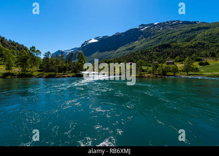 Emerald fjord among mountains covered with green trees, white snow and waterfalls. Norway, around Stryn. Stock Photo