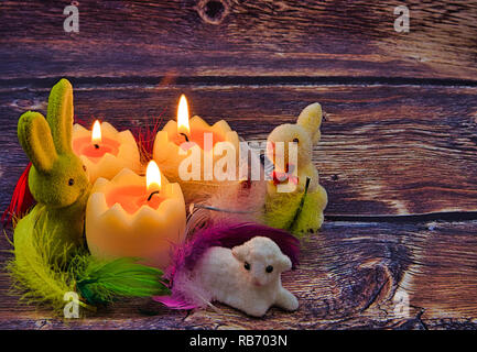Romantic Easter composition with burning candles, bunnies and Easter lamb in colorful feathers in vintage style Stock Photo