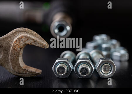 Screws, nuts and keys on a workshop table. Tools and accessories for mechanics. Black background. Stock Photo