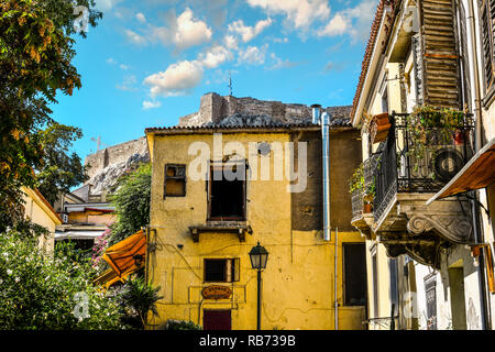 Broken hollowed out windows in an old building at the base of the Acropolis Hill as the Greek Flag flies on the historic Acropolis in Athens Greece Stock Photo