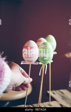 A beautiful close-up of 3 easter eggs on sticks over tables with a woman hand holding them and an amazing depth of field as background Stock Photo