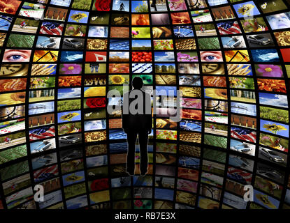 spherical room with a wall of television screens and a man standing on a reflective floor looking at it Stock Photo