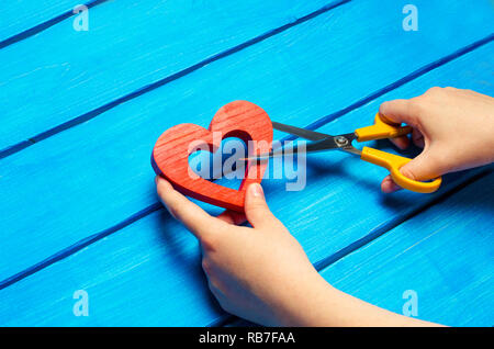 girl cuts the heart with scissors, the concept of breaking relations, quarrels and divorce. Betrayal of the othere. blue background Stock Photo
