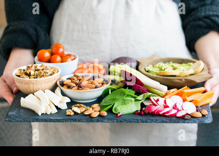 Woman holding healthy meal selection of clean organic foods: vegetables, nuts, avocado, almonds, green leaves Stock Photo