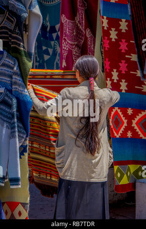 OTAVALO, ECUADOR, NOVEMBER 06, 2018: Back view of indigenous woman wearing andean traditional clothing and selling some products in the street market in the city of Otavalo Stock Photo