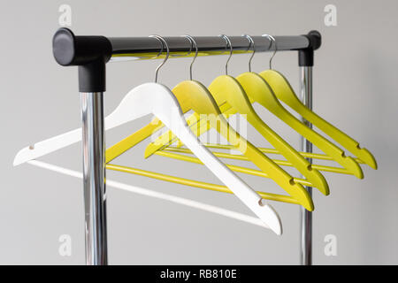 Empty clothes hangers on metal rail against grey background. Rectangular metal clothing rail with empty color wooden coat hangers. Stock Photo