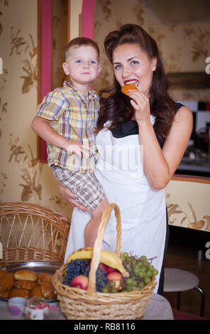Mother and son in the kitchen with pastries other food. Studio shot, home interior. Stock Photo