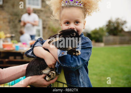 Little girl excited while stroking a pet rabbit ourdoors at a easter garden party. Stock Photo