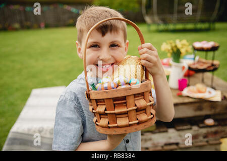 Young boy standing outdoors holding a basket full of chocolate easter eggs that he found on the easter egg hunt. Stock Photo