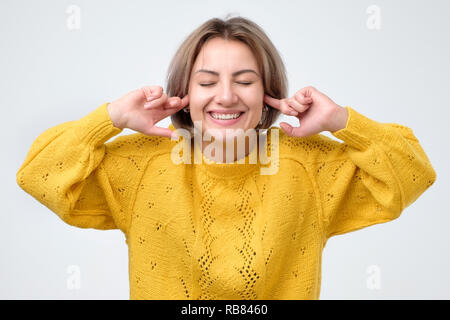 Beautiful casually dressed young european woman with mysterious smile and playful expression on her face, plugging ears, pretending not to hear what s Stock Photo