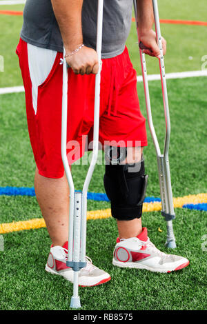 An injured player is on the sidelines wearing a knee brace and using crutches after he has had knee surgery. Stock Photo