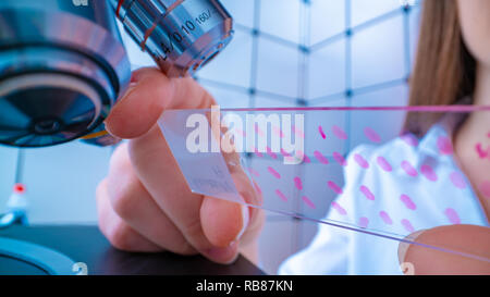 Scientist analyzing microscope slide at laboratory. Young woman technician is examining a histological sample, a biopsy in the laboratory of cancer re Stock Photo