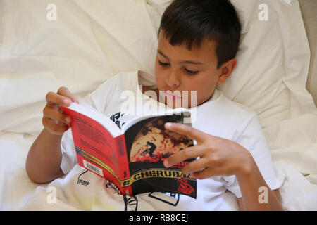 11-year-old boy reading in bed in Salento, Italy. Stock Photo