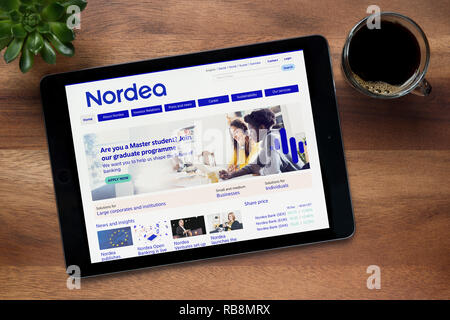 The website of Nordea bank is seen on an iPad tablet, on a wooden table along with an espresso coffee and a house plant (Editorial use only). Stock Photo