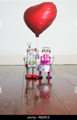 two robots in love  bouth holding a red balloon standing on a old wooden floor Stock Photo