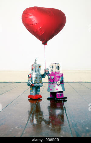 two robots in love holding a red balloon standing on a old wooden floor Stock Photo