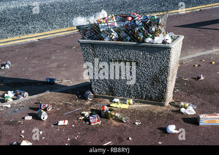 A rubbish container over-flowing with rubbish.Rubbish on the pavement and the road.A scene in a holiday resort on the west coast of England. Stock Photo
