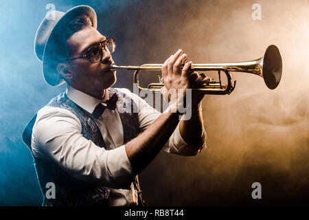 young jazzman playing on trumpet on stage with dramatic lighting and smoke Stock Photo