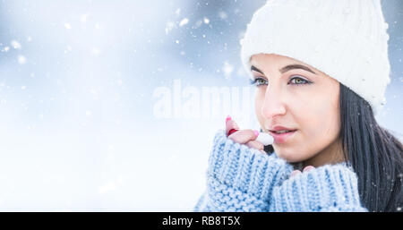 Attractive young woman l protecting lips with lip balm in snowy and frozen weather. Stock Photo