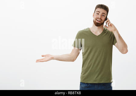 Hey happy receive call from you mate. Portrait of pleased young attractive bearded guy talking on smartphone and extend hand sideways as being surprised and glad to chat against white background Stock Photo