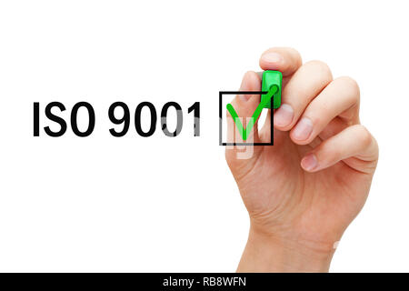 Hand putting verification check mark on ISO 9001 Quality Management System certification with green marker. Stock Photo