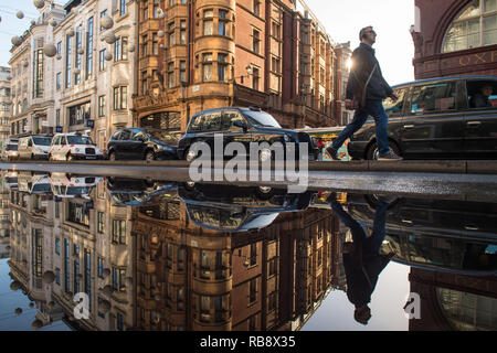 Taxis and pedestrians are reflected in standing water on Oxford Street, London, following a burst water main in one of the capital's busiest shopping streets. Stock Photo