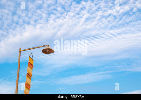 Vintage lamp on top of bamboo pole and yellow lanna flag(Tung) on the blue sky in the morning. Stock Photo