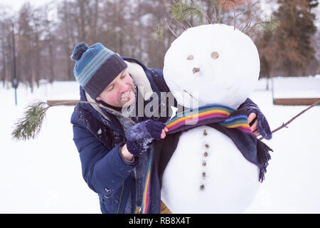 Young european man in warm clothes making snowman from snow outdoor. Having fun like a child at winter vacation. Stock Photo